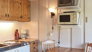 A compact kitchen with wooden cabinets, a stove, a microwave, a coffee maker, and a dining table with two chairs. - 4 Person Holiday Home in Folkestad (Volda)