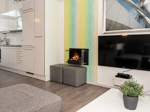 A modern living room with a flat-screen TV, a fireplace, and a kitchen area with white cabinets.