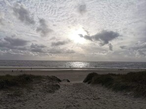 A beach with a sandy path leading to the water, under a cloudy sky.