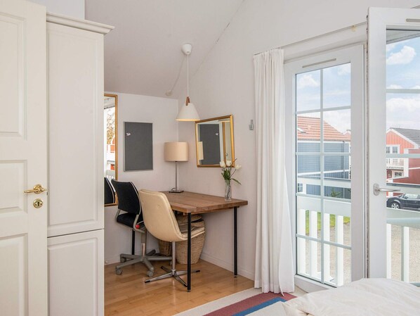 A room with a wooden desk, a chair, a lamp, a mirror, and a view of the outside through a glass door.