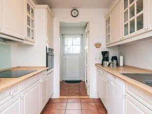 Une cuisine étroite avec des meubles blancs, un plan de travail noir, une machine à café et une horloge au mur.