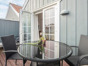 A glass-top table with chairs on a wooden deck, a door leading to a covered area, and a potted plant with flowers. - 4 Star Holiday Home in Blavand (Blavand)