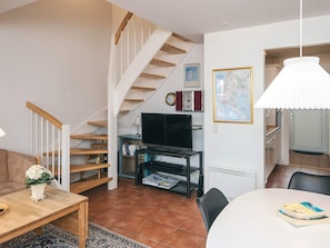 A living room with a staircase, a television on a stand, a dining table with chairs, and a map on the wall. - 4 Star Holiday Home in Blavand (Blavand)