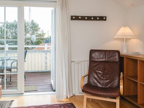 A room with a brown leather chair, a white lamp, a wooden shelf, and a view through a glass door to an outdoor area with a patio.
