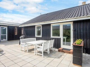 A patio with a table and chairs, a barbecue grill, and a planter with plants.