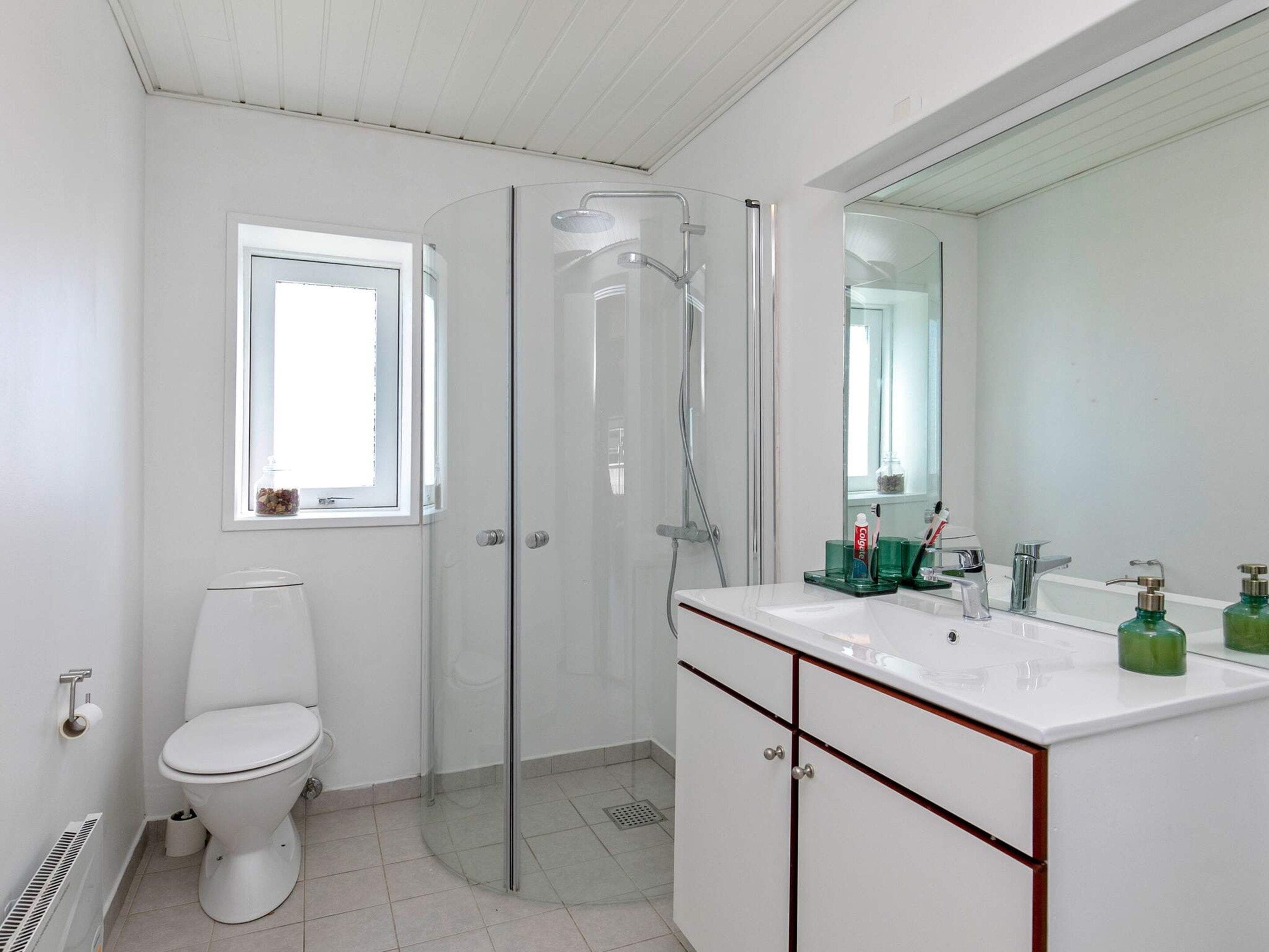 A modern bathroom with a toilet, a glass shower enclosure, a sink with a mirror, and toiletries.