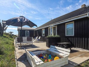 A house with a patio, outdoor seating, and a sandbox with toys.