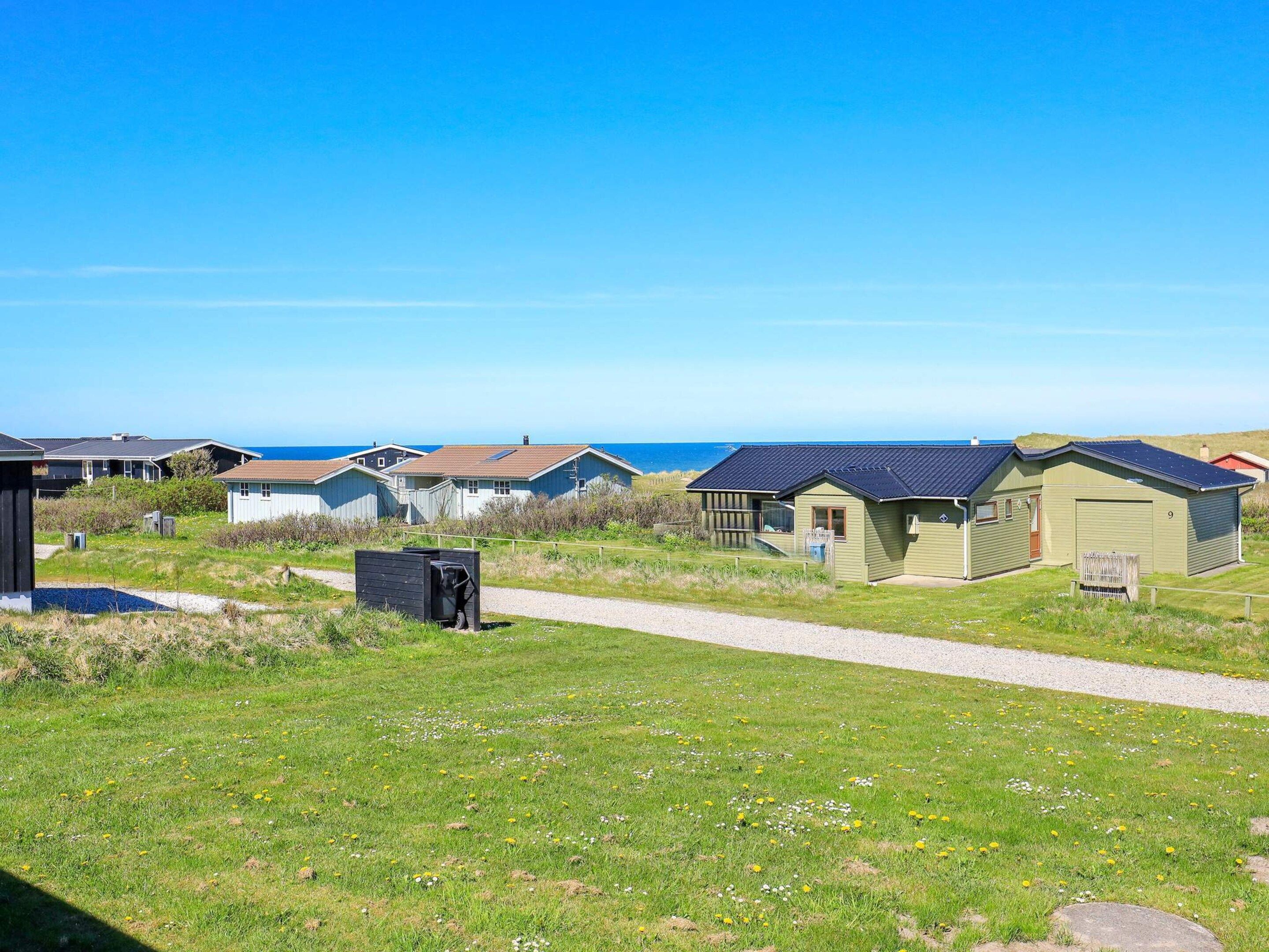 A row of beachside cabins with a gravel path leading to them, set against a clear sky and ocean view.