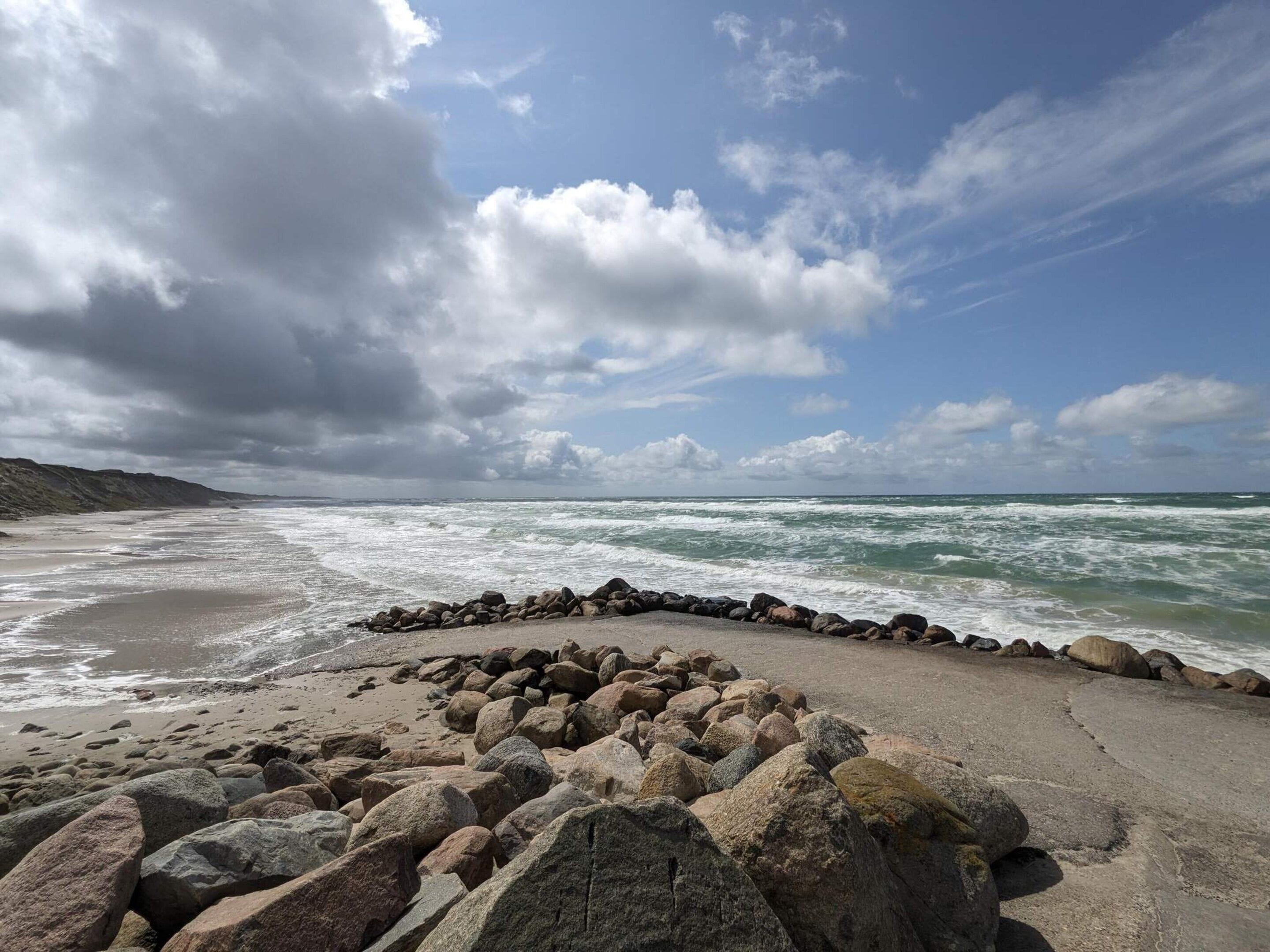 A rocky beach with waves crashing onto the shore and a cloudy sky above.