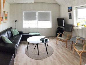 A living room with a black leather sofa, a round coffee table, a wooden chair, a television, and a window with blinds.