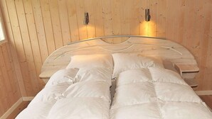 A bed with white bedding in a room with wooden walls and two wall-mounted light fixtures.