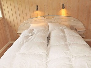 A bed with white bedding in a room with wooden walls and two wall-mounted light fixtures.