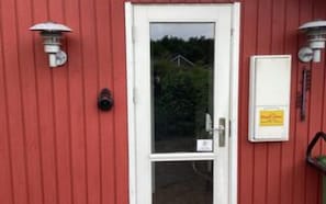 Un bâtiment rouge avec une porte blanche, une boîte aux lettres et deux lampes fixées au mur.