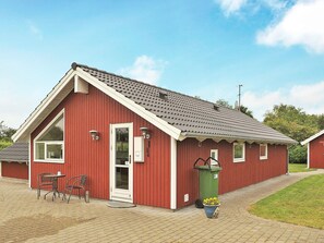 Un bâtiment rouge avec un toit en pente, une porte et un petit espace extérieur aménagé avec des chaises et une table.