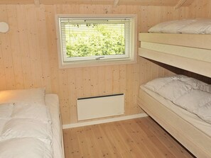 Une pièce aux murs en bois, une fenêtre avec des stores, des lits superposés et un radiateur.