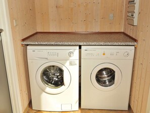 Deux machines à laver à chargement frontal se trouvent dans une buanderie dont les murs sont en bois et le plan de travail en granit.
