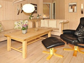 Een houten eettafel met een bank, een zwarte lederen stoel en een bank met bloemkussens in een kamer met houten wanden en een grote spiegel.