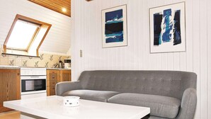 En moderne stue med en grå sofa, et hvidt sofabord og et køkken i baggrunden.