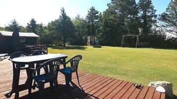 A wooden deck with a table and chairs, a swing set, and a grassy yard.