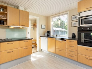A modern kitchen with wooden cabinets, a black countertop, a microwave, and a stove. - 4 Star Holiday Home in Nibe (Nibe)
