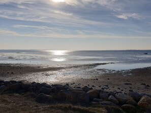 Ein Strand mit steiniger Uferböschung und ruhigem Wasser, das die Sonne spiegelt.