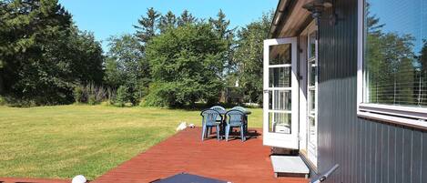 A patio with a table and chairs, a sun lounger, and a building with a large window.