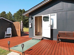 Um deck de madeira com um banco, uma porta que dá para um quarto e uma cadeira em frente a um edifício.