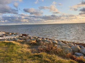 Eine Küstenlandschaft mit felsigem Ufer, grünen Flächen und ruhigem Meer unter einem teils bewölkten Himmel.
