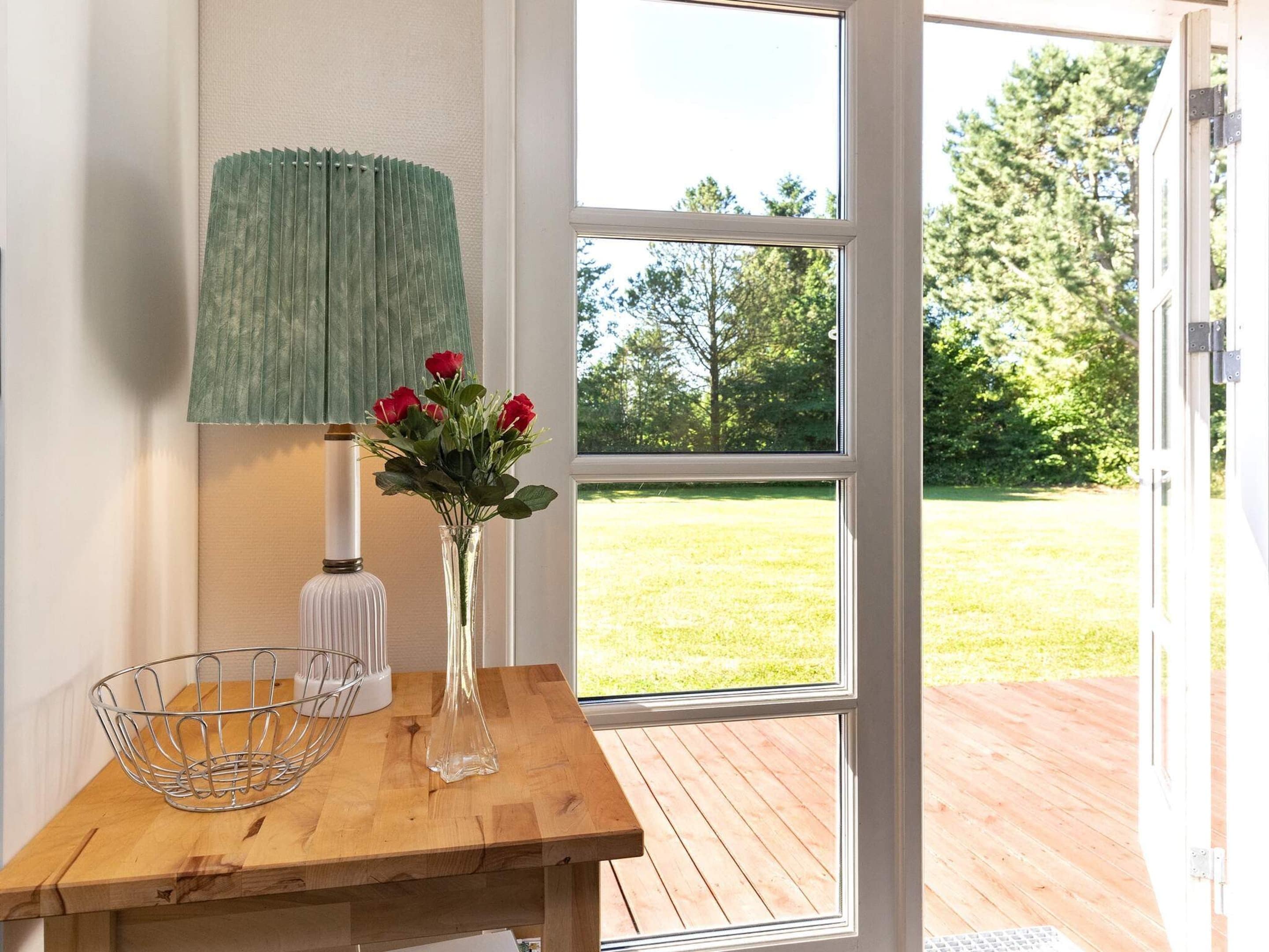 A wooden table with a metal basket, a white vase with red flowers, and a green lamp.