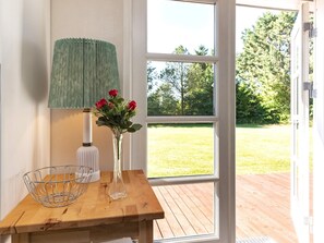 Ein Holztisch mit einem Metallkorb, einer weißen Vase mit roten Blumen und einer grünen Lampe.