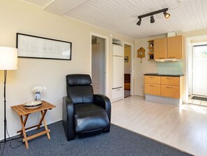 Ein Zimmer mit einem schwarzen Ledersessel, einem kleinen Holztisch mit einer Schale, einem gerahmten Bild an der Wand und einer Küchenzeile mit Holzschränken und einem Fenster.