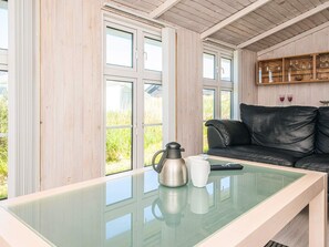 A room with a glass-top table, a black leather sofa, and a wooden cabinet with glass doors.