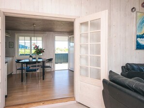 A room with a dining table, chairs, a black leather couch, and a large window with a view. - 4 Person Holiday Home in Ringkobing (Ringkobing)