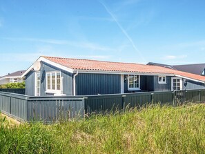A single-story building with a red-tiled roof, a satellite dish, and a fenced yard. - 4 Person Holiday Home in Ringkobing (Ringkobing)