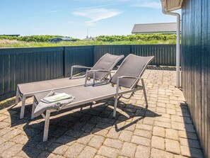 Een terras met een lounge stoel met metalen frame en een kleine tafel, een houten hek en een gebouw op de achtergrond.