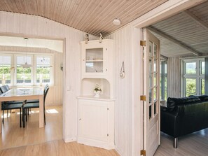 Een kamer met een eettafel, stoelen, een zwarte leren bank en een witte kast met planken.