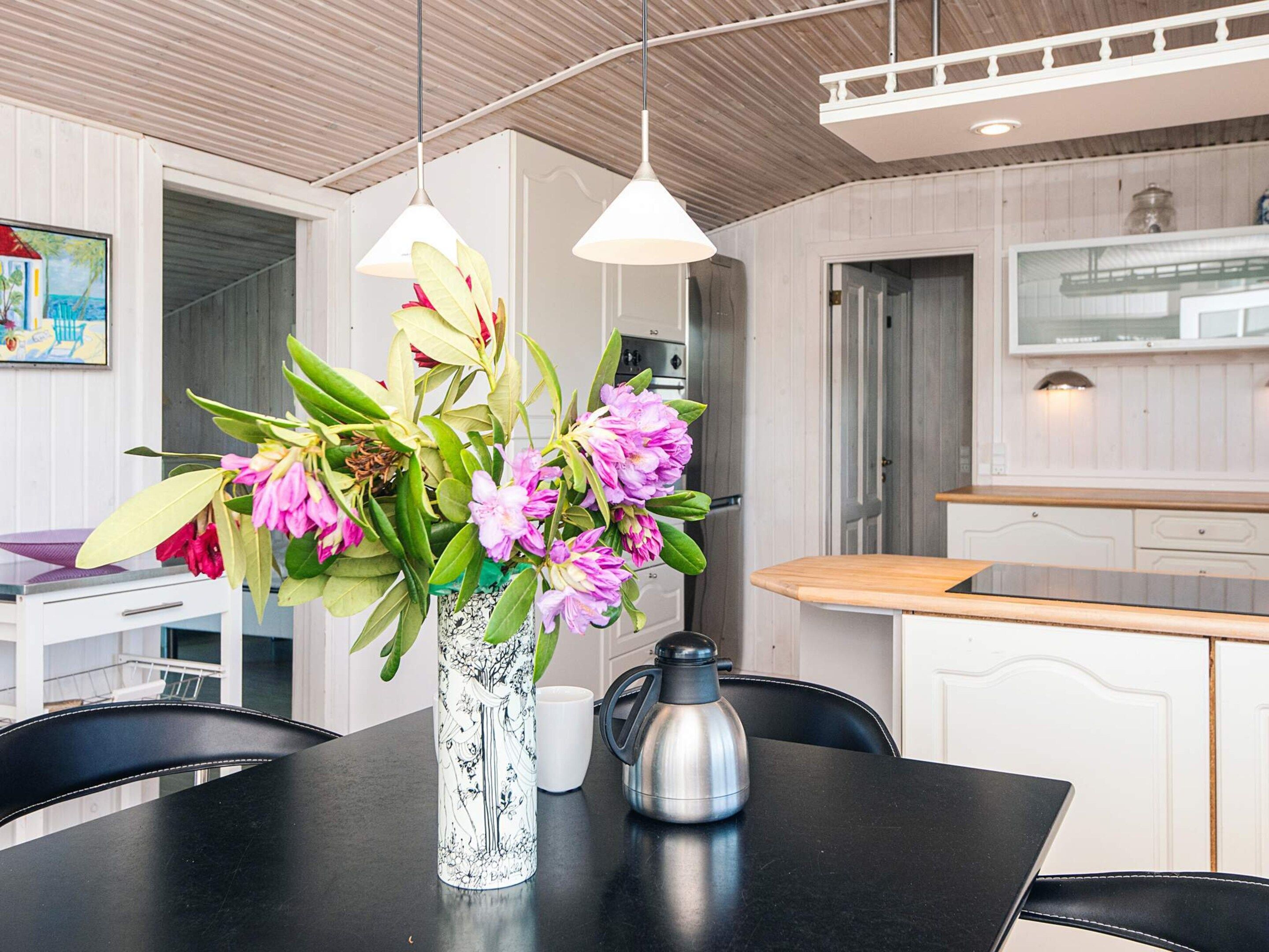 A modern kitchen with white cabinetry, a black dining table, and a vase with flowers.