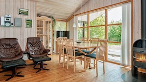 A cozy cabin interior with wooden floors, a dining area with a table and chairs, leather armchairs, a television, and a fireplace. - Inviting Holiday Home in Ebeltoft near Sea (Ebeltoft)