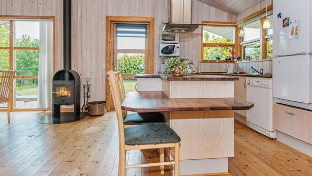 A modern kitchen with wooden floors, a central island, a built-in stove, and a large window overlooking greenery. - Inviting Holiday Home in Ebeltoft near Sea (Ebeltoft)