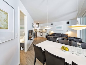 A modern kitchen with white cabinetry, a dining area with a white table, and a living area with a dark sofa. - Holiday Home in Wendtorf (Schönberg)