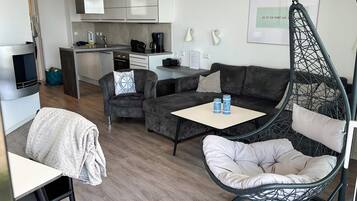 Un espacio habitable moderno con sofá, una silla colgante, una mesita y una cocina al fondo.