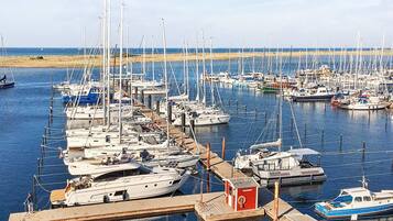 A marina with numerous boats docked, a small red building, and a sandy beach in the background.