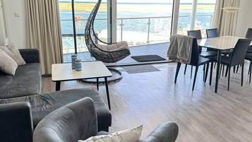 Een moderne woonkamer met een bank, een hangstoel, een eettafel met stoelen en uitzicht op zee.