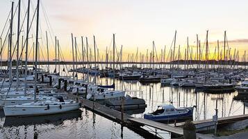 Ein Yachthafen mit mehreren angedockten Booten, ruhigem Wasser und einem Sonnenuntergang im Hintergrund.