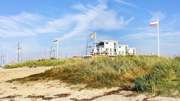 A coastal building with multiple flags, surrounded by dunes and wind turbines.