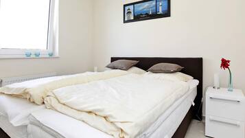 A bedroom with a bed, pillows, a nightstand, a vase with a flower, and a framed picture on the wall.