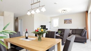 A modern dining area with a wooden table, black leather chairs, a vase with flowers, and a bottle of wine. - Holiday Home in Grossenbrode (Grossenbrode)
