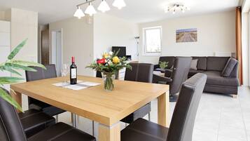 Un comedor moderno con una mesa de madera, sillas de cuero negro, un florero con flores y una botella de vino.