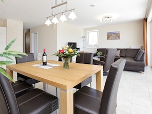 A modern dining area with a wooden table, black leather chairs, a vase with flowers, and a bottle of wine. - Holiday Home in Grossenbrode (Grossenbrode)