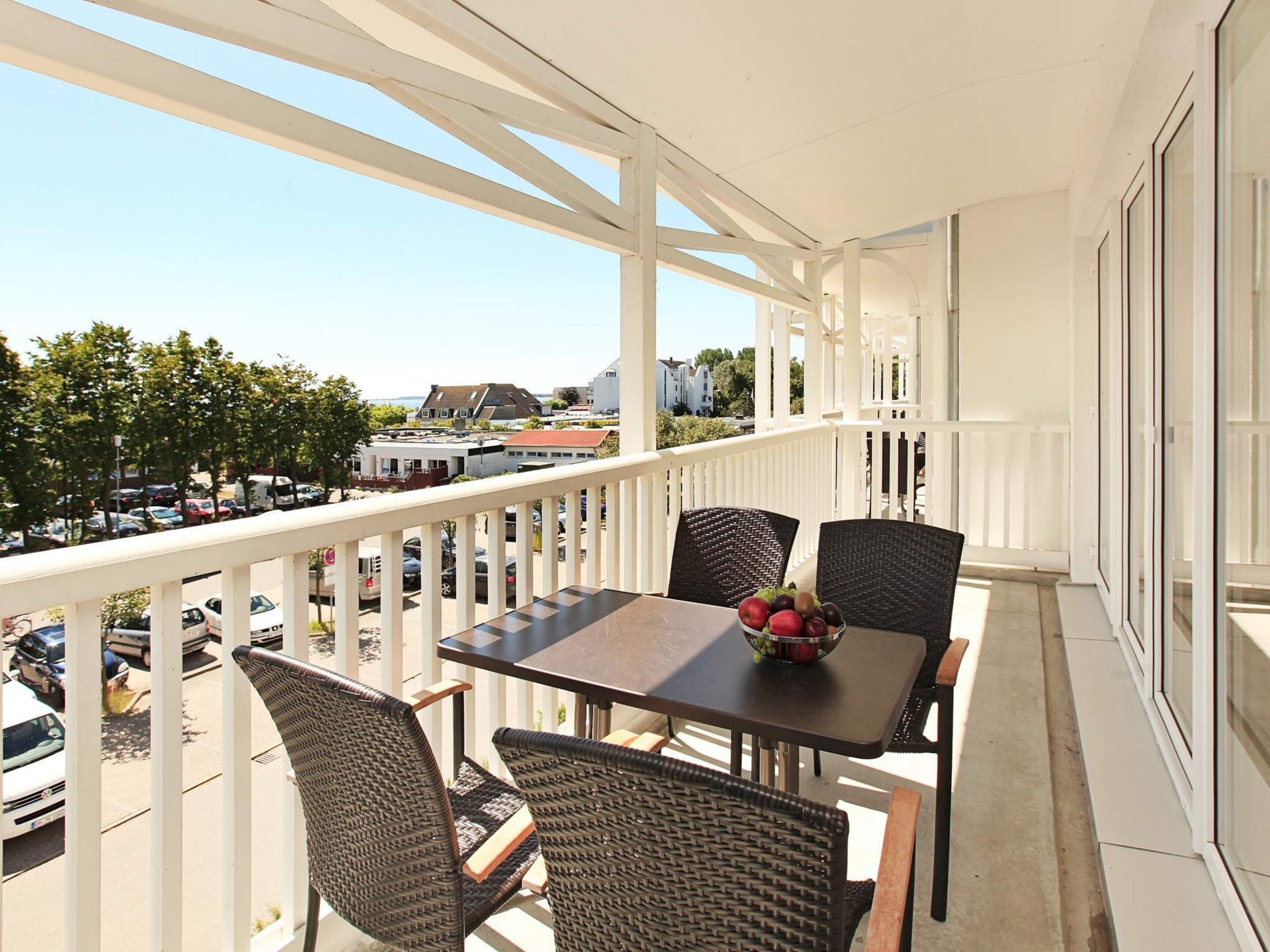 A balcony with a table and chairs, a bowl of fruit, and a view of the street and buildings.